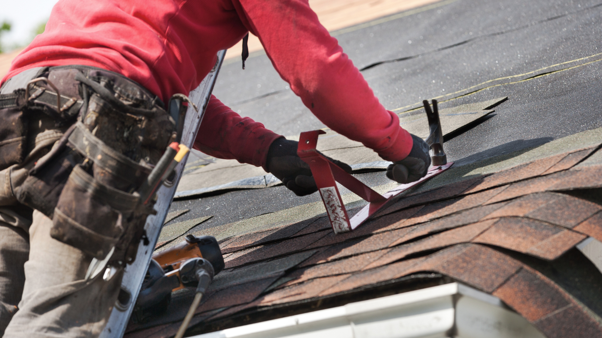 Roofing contractor in a red hoodie measuring and installing architectural asphalt shingles on a residential roof
