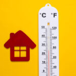 Weather thermometer and house figurine on yellow background.