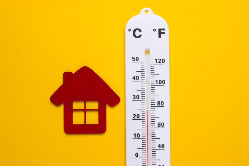 Weather thermometer and house figurine on yellow background.