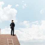 Young determined businessman standing with back on house roof and looking away.